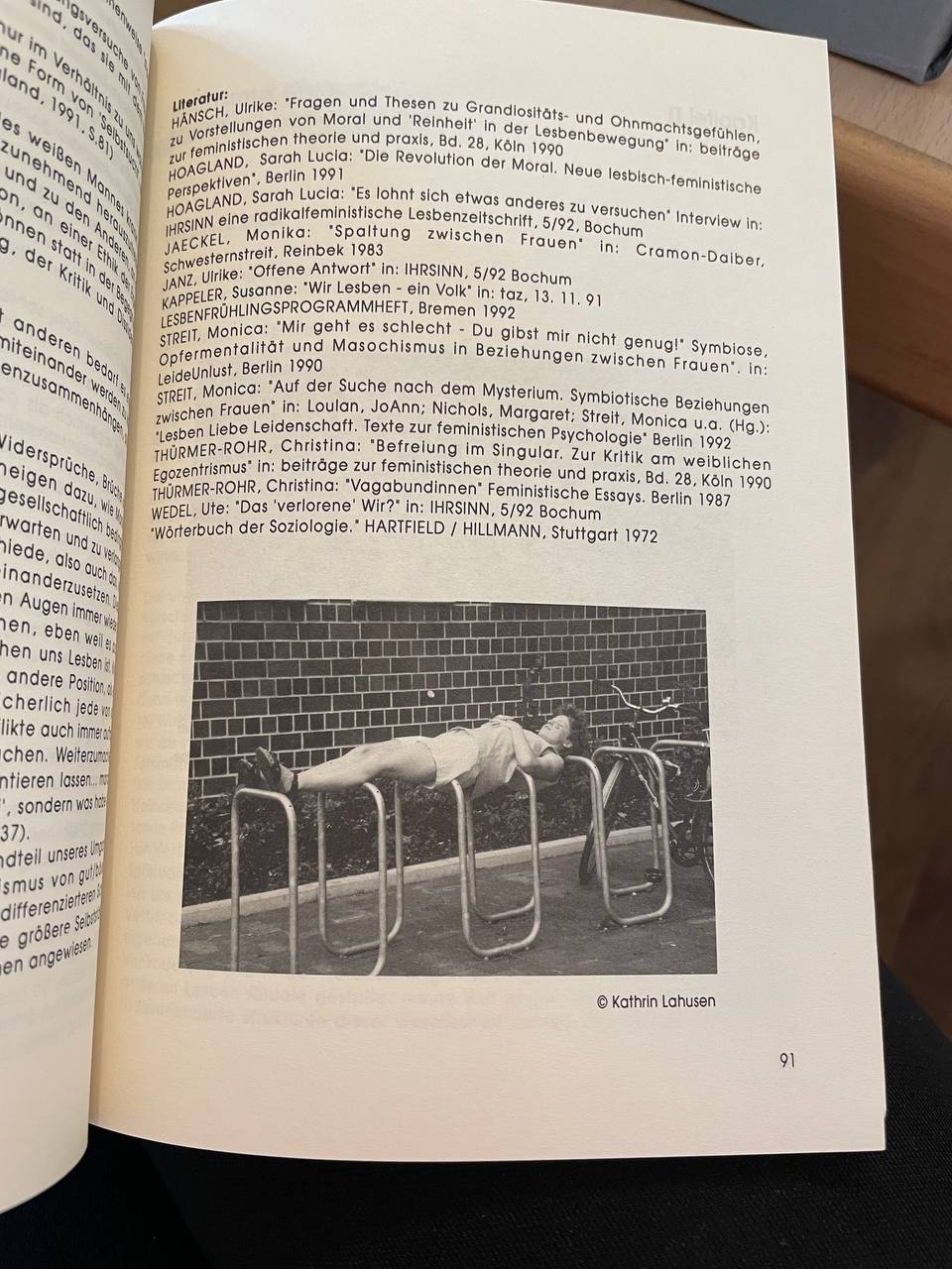 Eine abfotografierte Buchseite aus den Recherchen im Belladonna-Archiv Bremen. Auf der Seite sind Fußnoten zu sehen sowie ein Bild, auf dem eine weiblich gelesene Person steif wie ein Brett auf einem Fahrradständer liegt.